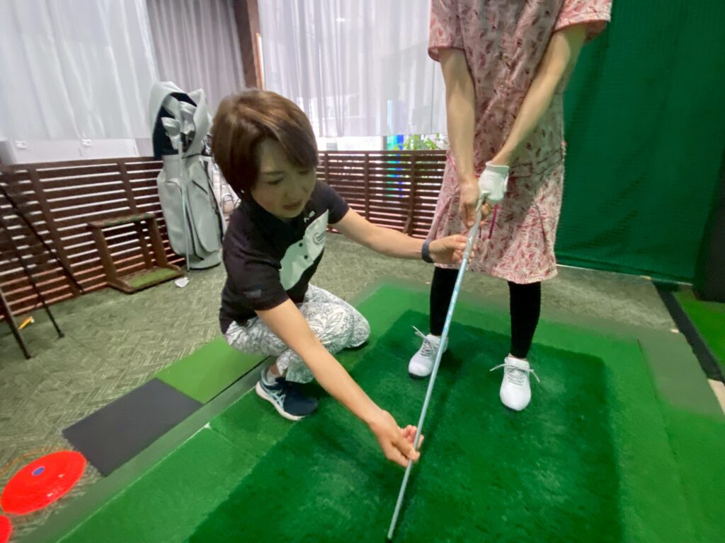 ゴルフクラブの持ち方を教わっている初心者ゴルファーの女性とプロのインストラクター